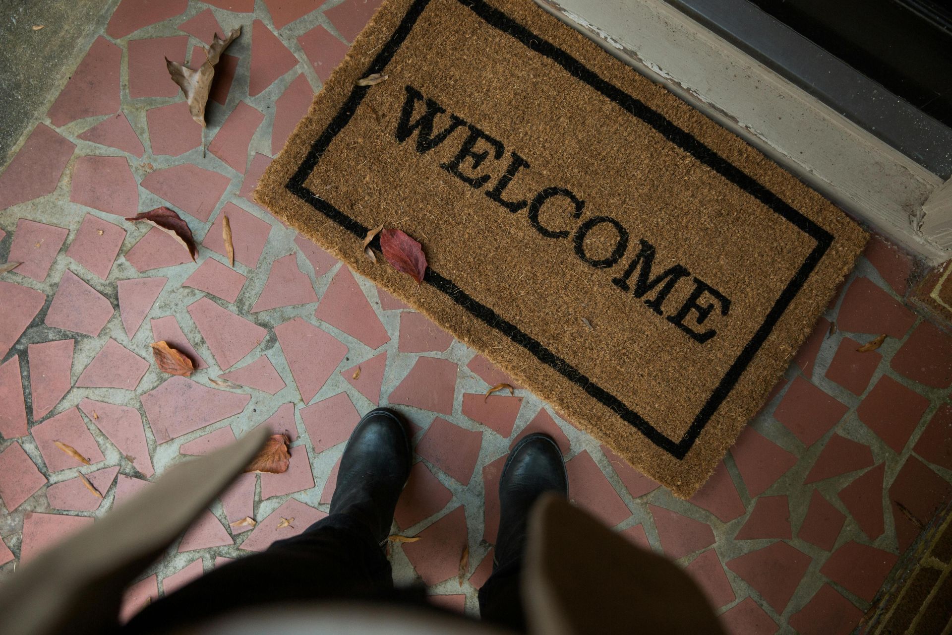 Welcome mat on a tiled porch with boots visible. Perfect for home decor or hospitality themes.